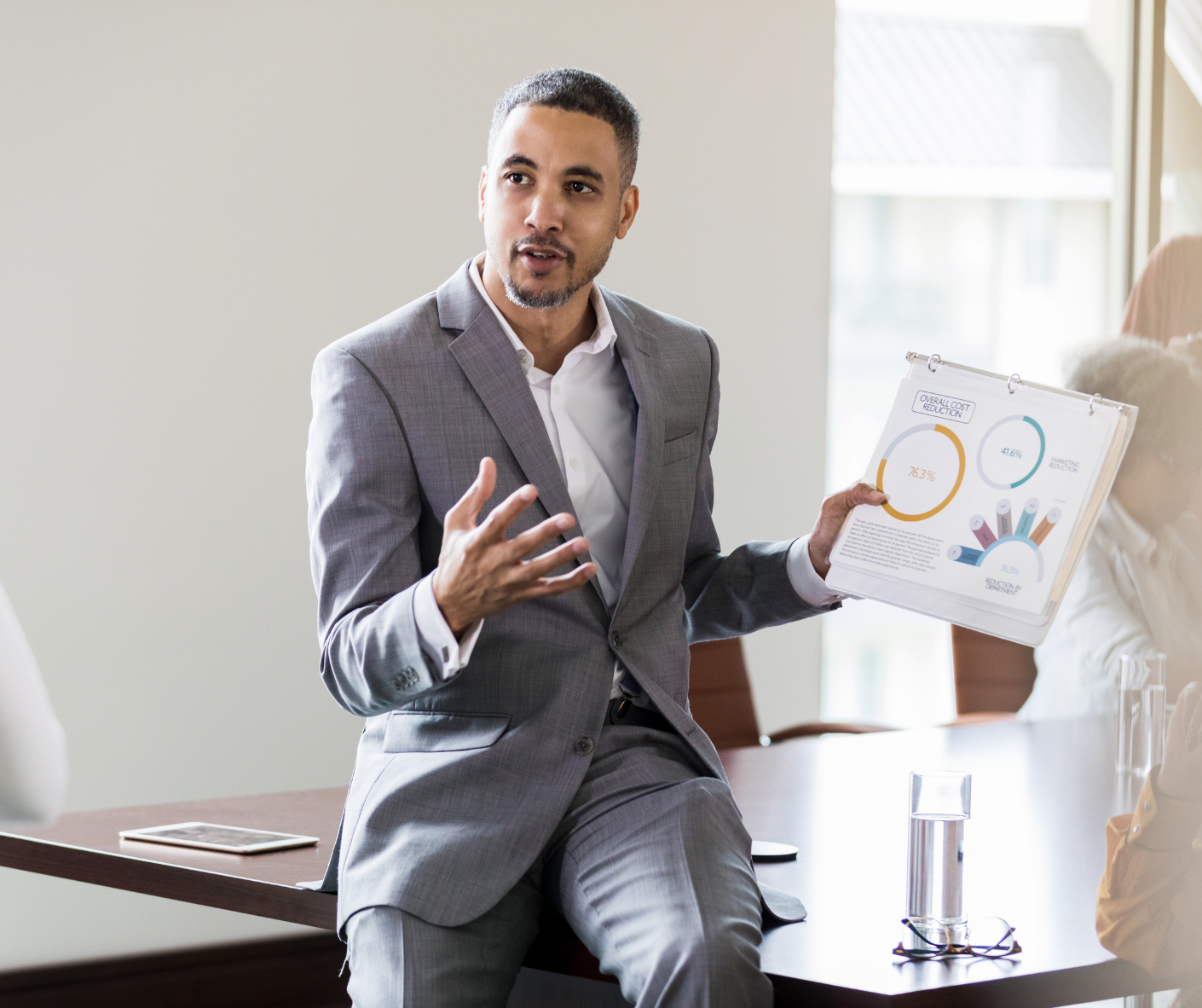 Executive in a gray suit explaining a chart to colleagues in a conference room