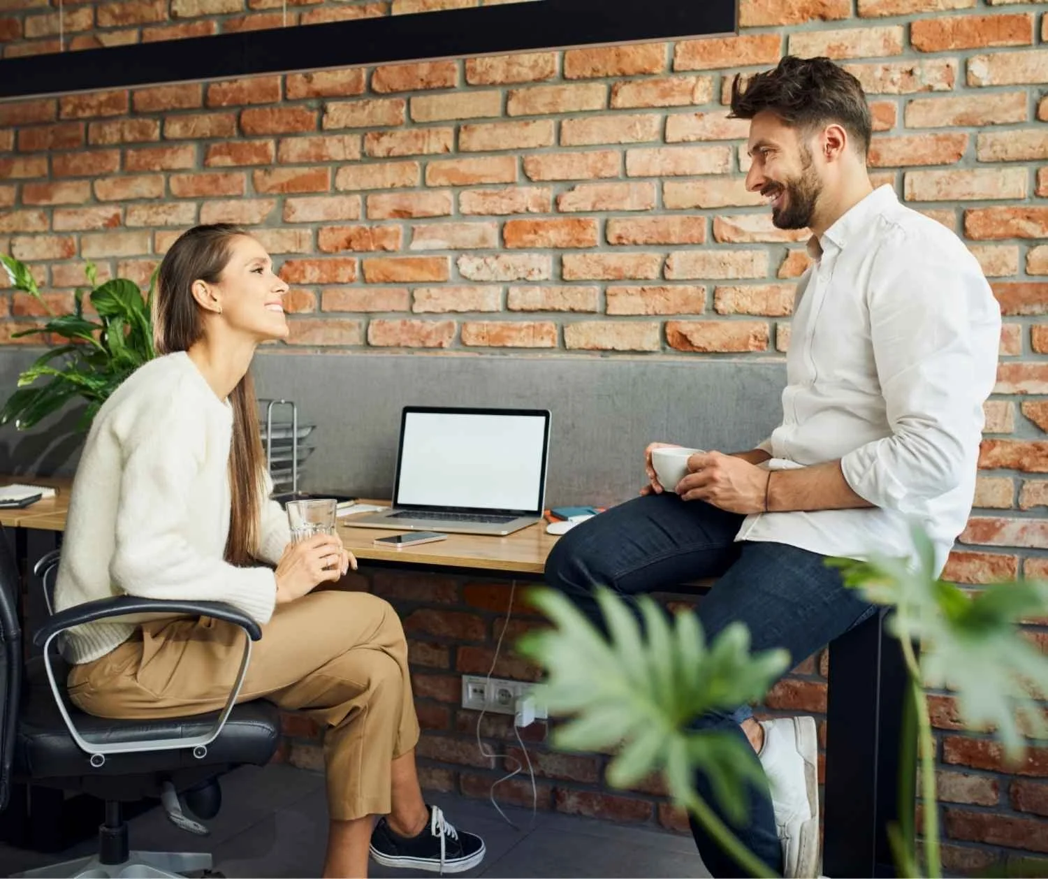 two coworkers talking at a bright office desk, one leading, relaxed and friendly