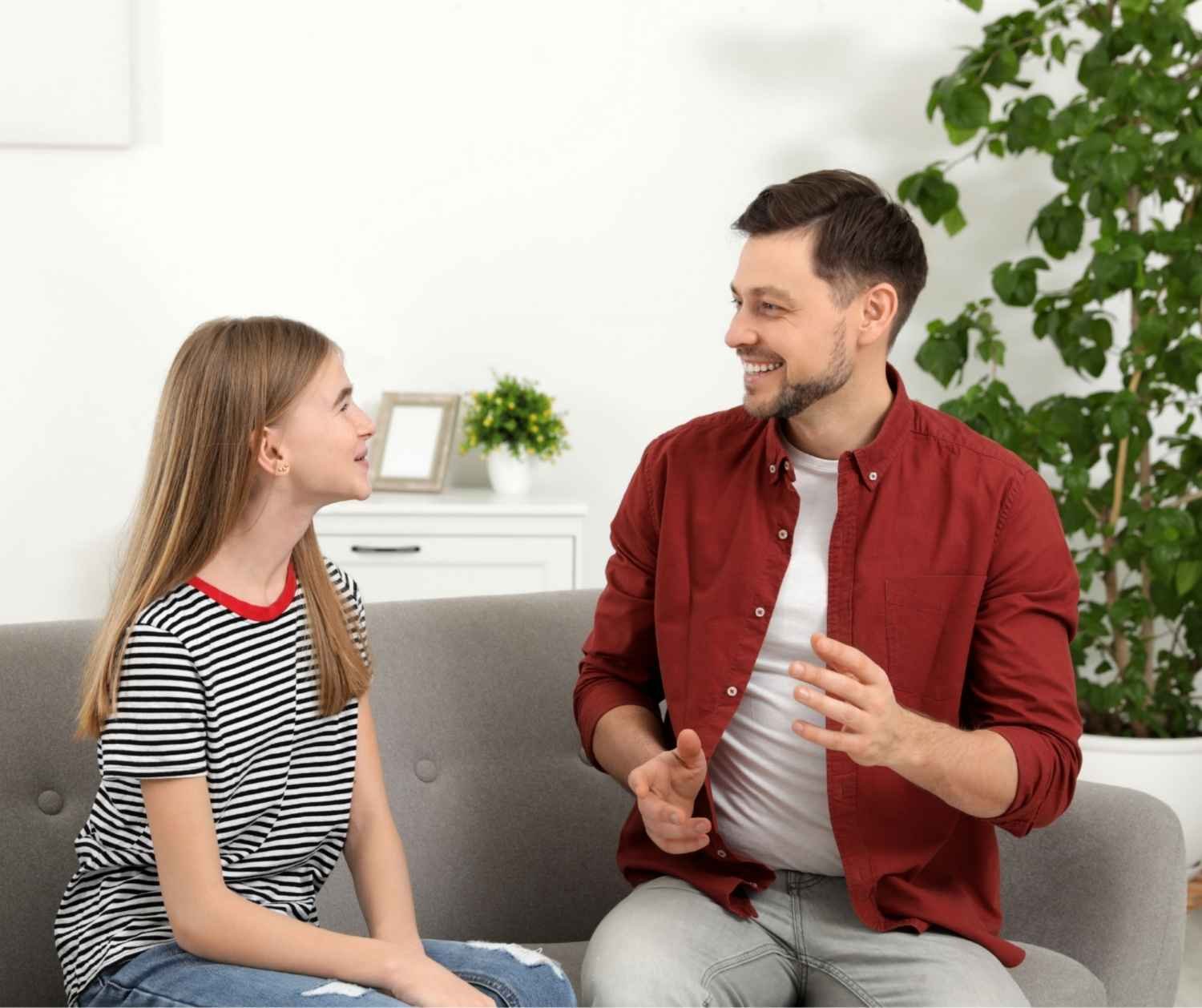 Father and teenage daughter talking together on a sofa at home.