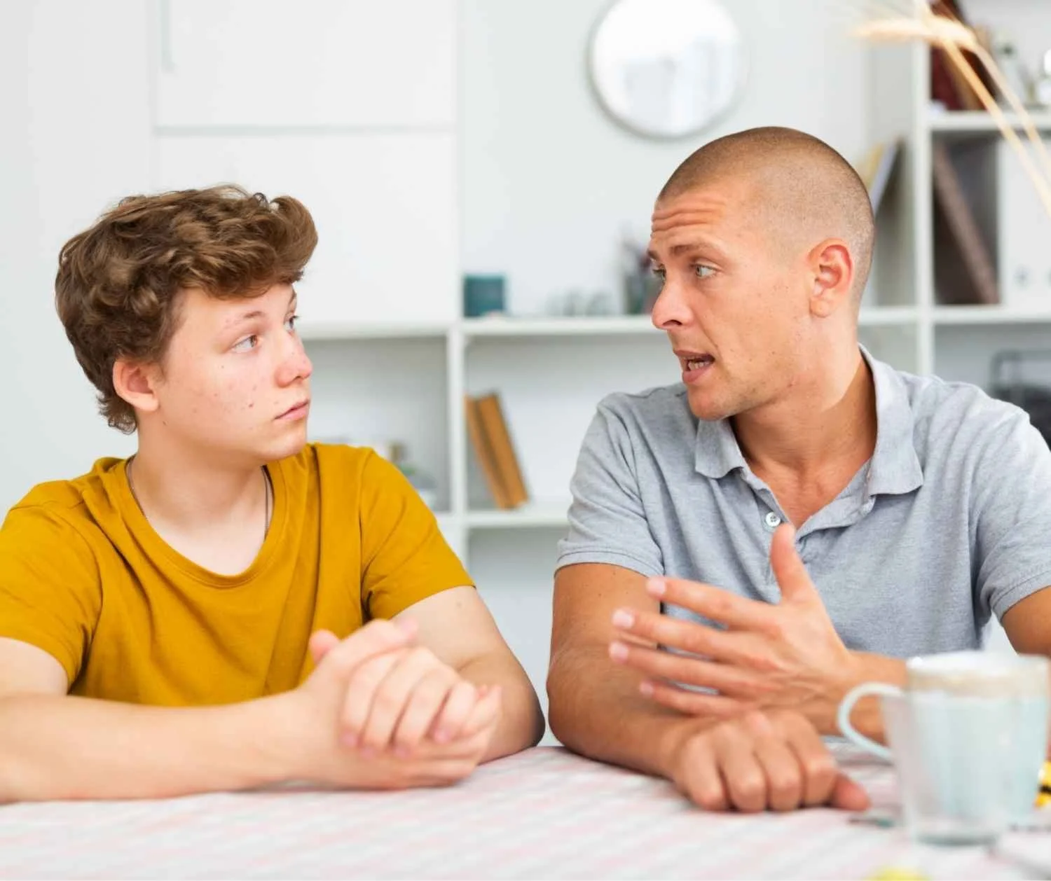 A father and his adult son talking at a kitchen table.