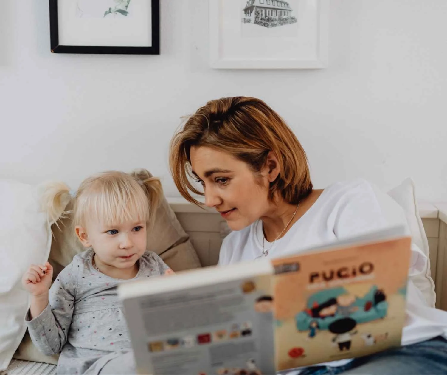 A mother reading a picture book with her toddler on the couch.