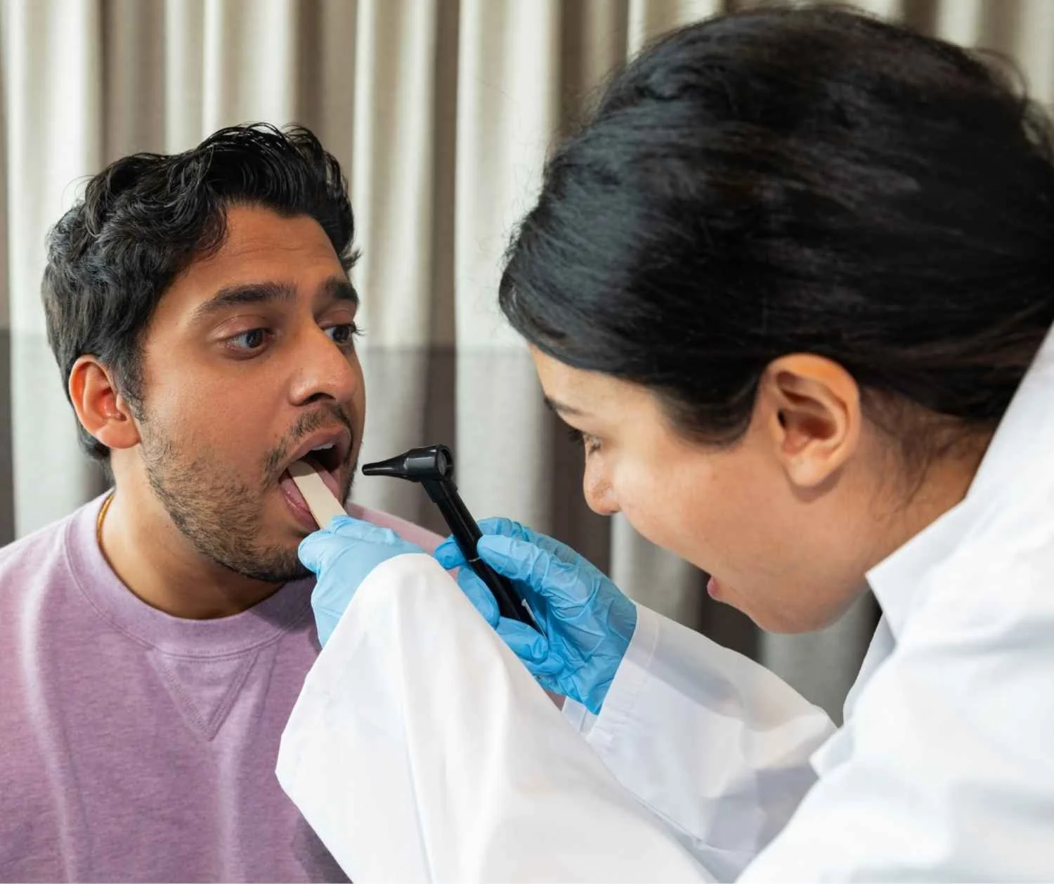 ENT doctor examining adult man throat, exam room