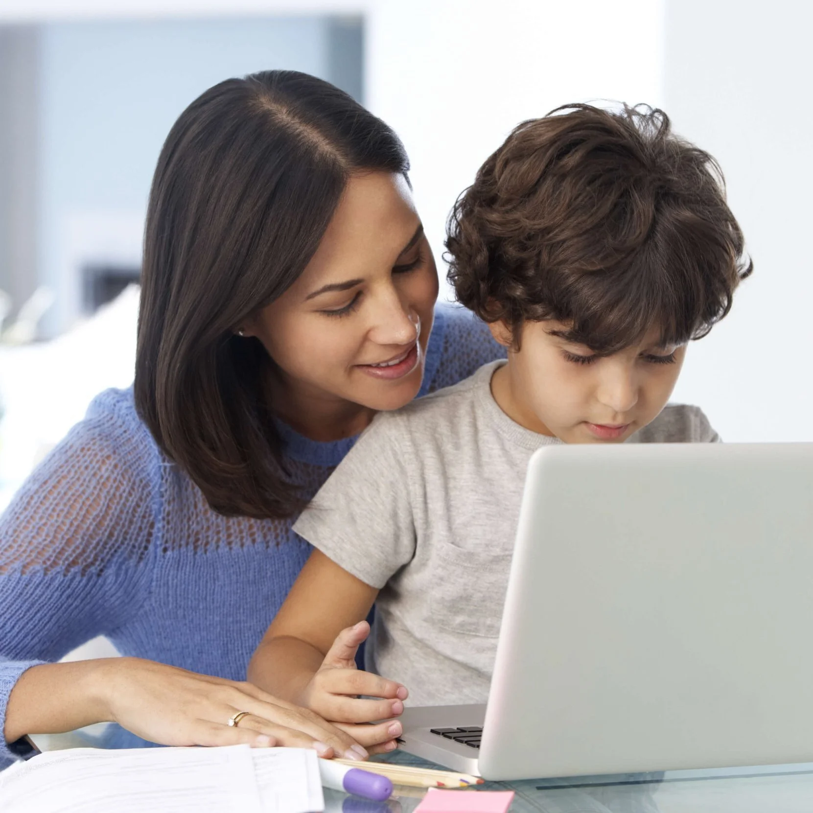 a mother helps her 6 year old son use a laptop for online therapy