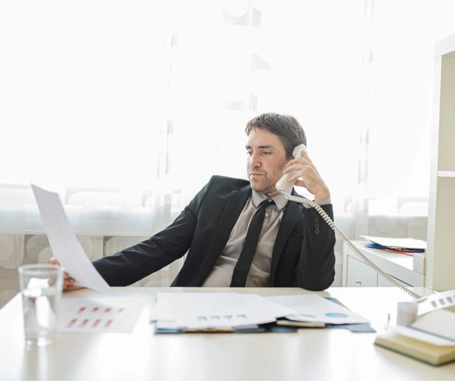 Man pausing mid phone call at his desk, looking unsure.