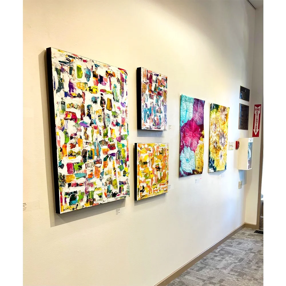 Abstract paintings displayed on a gallery wall, featuring vibrant colors and textured patterns.