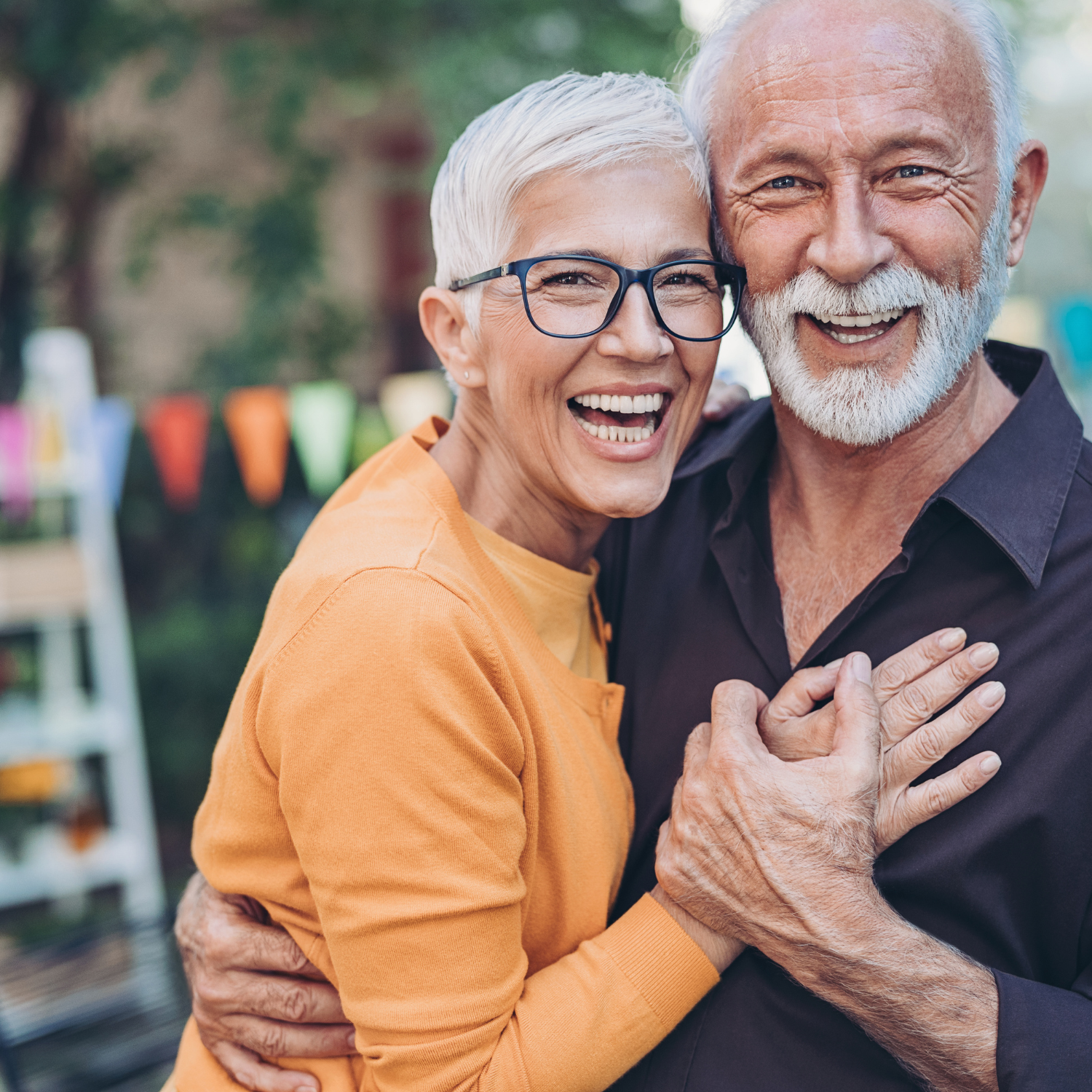 An elderly couple smiling and laughing together at an outdoor event, embracing each other.