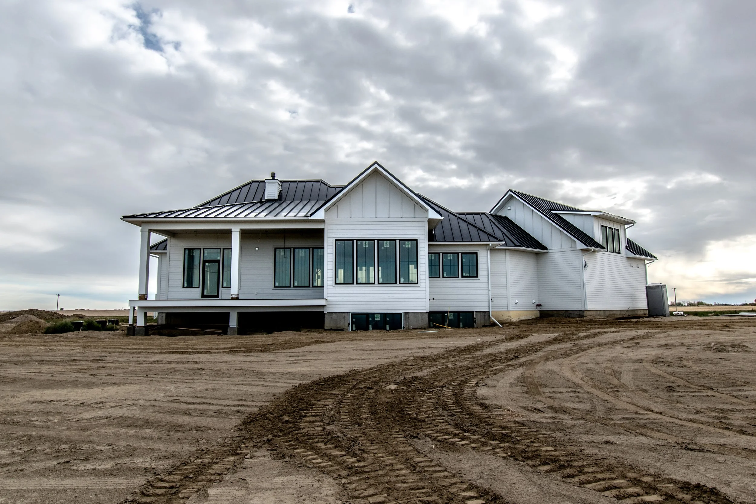 New white house under construction with dirt lot and tire tracks in front, cloudy sky overhead.