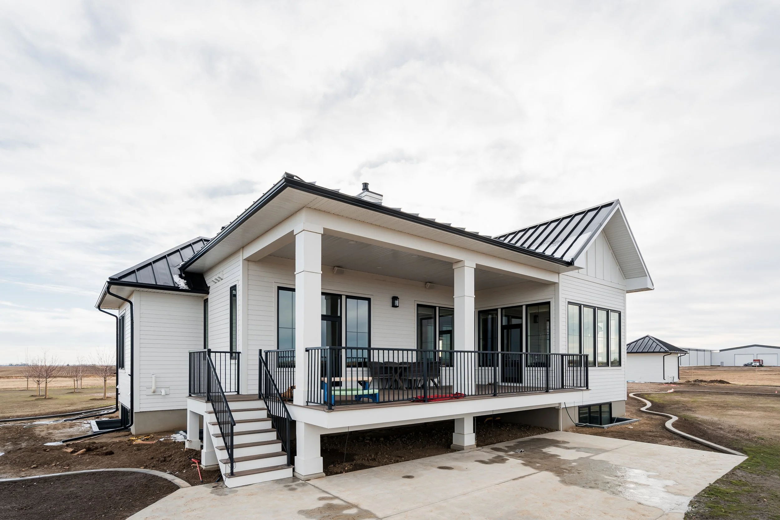 Modern white house with a screened-in porch, black railing, metal roof, and concrete driveway, under a cloudy sky.