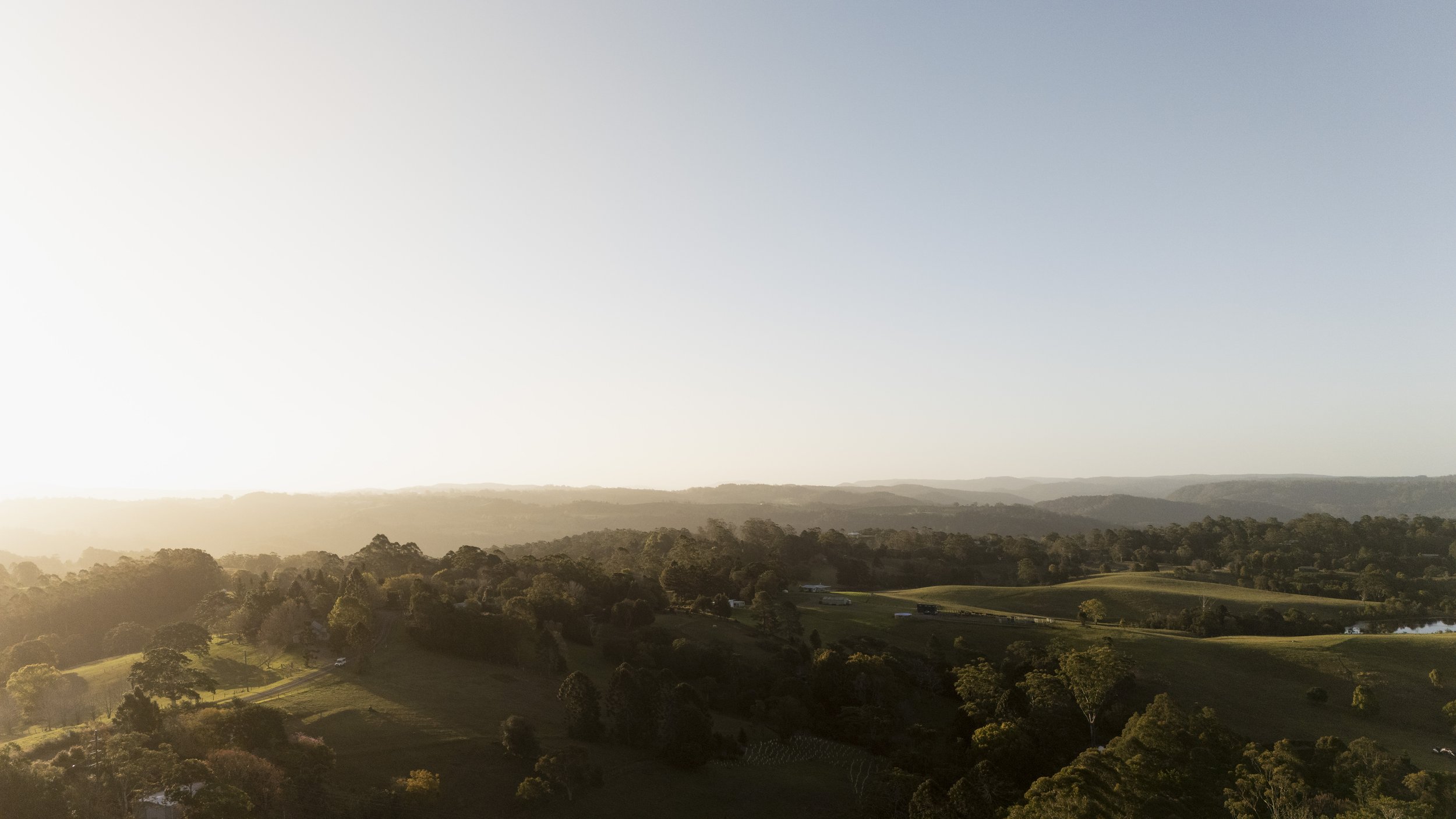 Sunset over rolling hills with trees and open fields, creating a peaceful landscape.