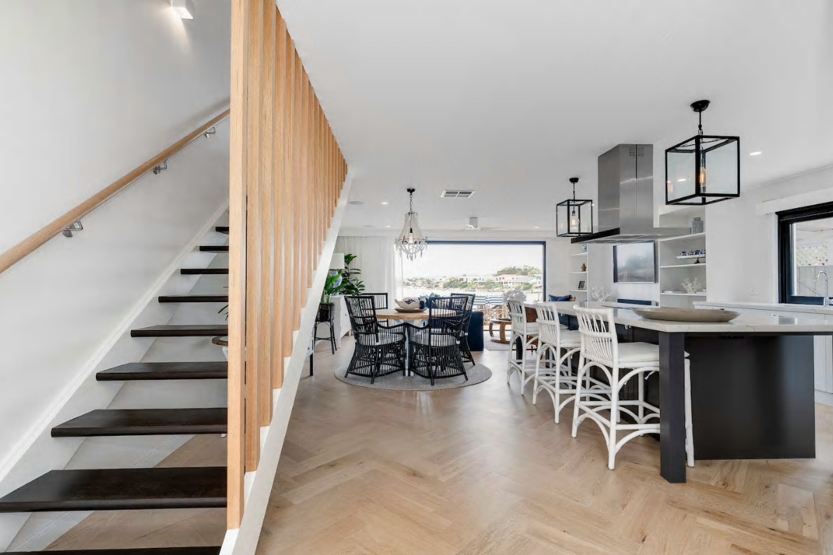 Open-concept living room and kitchen with wooden stairs, dining area, large window, and modern black and white decor.