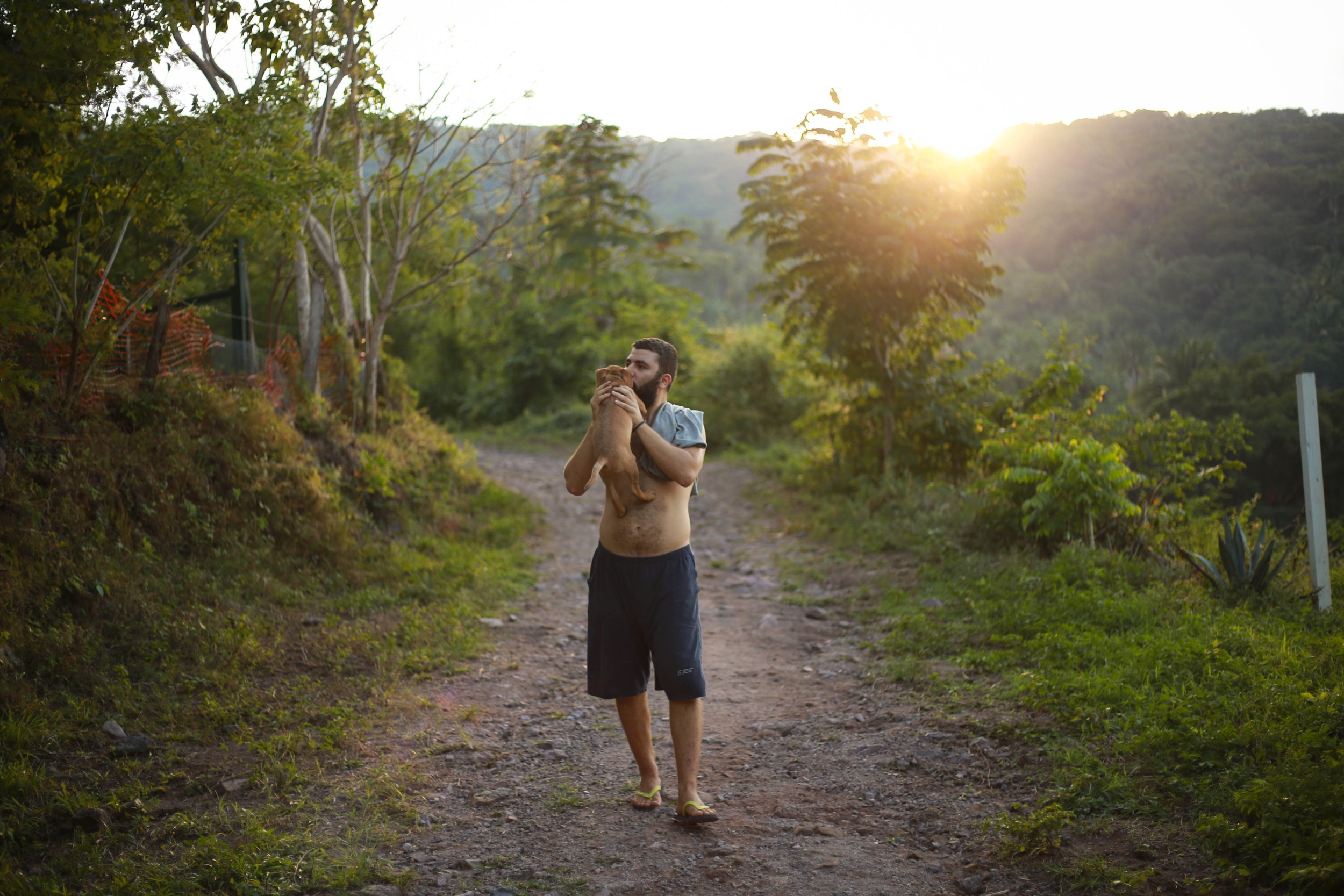 A man holding a dog on a dirt path surrounded by trees during sunset.