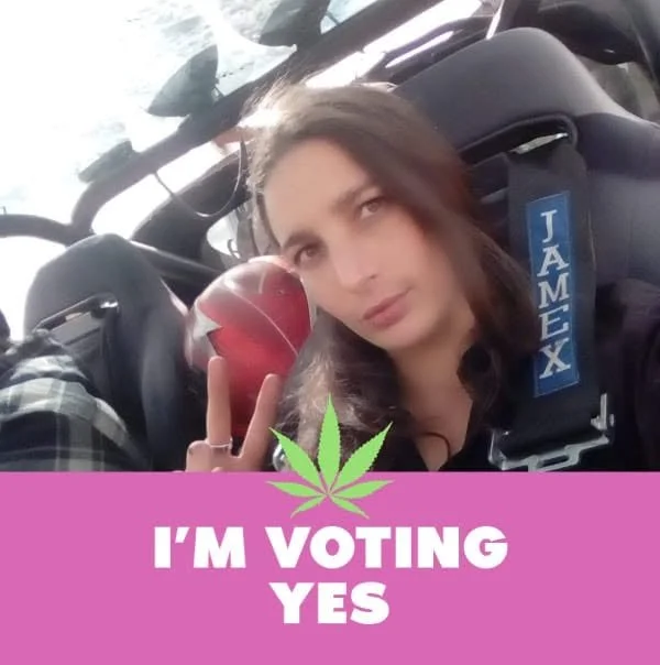 Young woman with long hair making a peace sign inside a small aircraft, holding a red apple, with a pink banner at the bottom that says 'I'm voting yes' and a green cannabis leaf above the text.