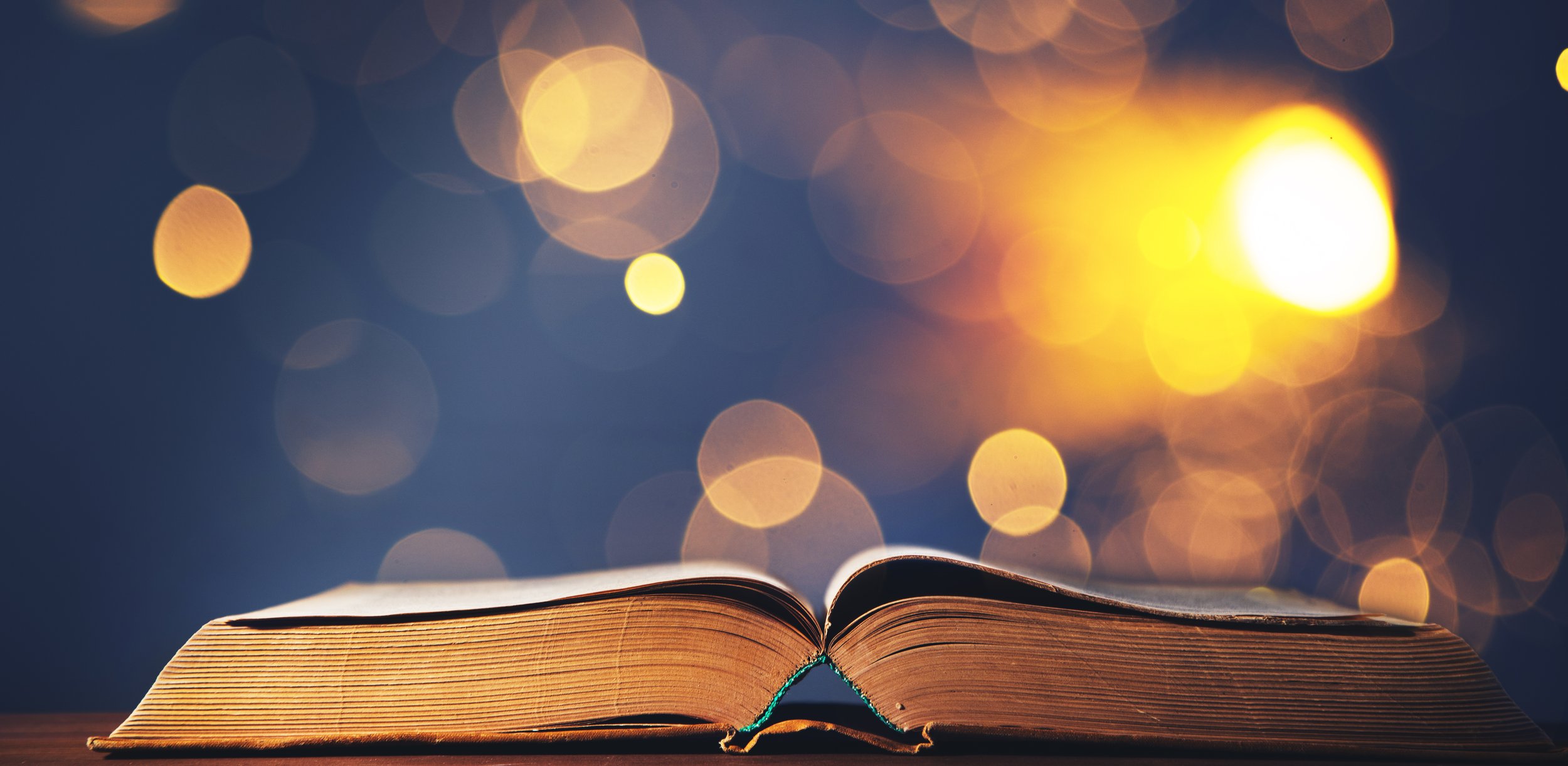 Open book on a table with a blurred background of warm glowing lights or bokeh effect.