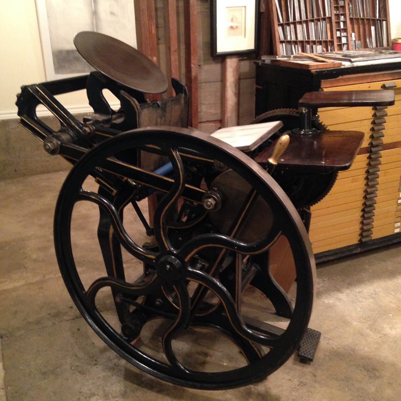 Vintage mechanical calculating machine with large black wheels and brass accents, located in a room with wooden furniture and framed pictures.