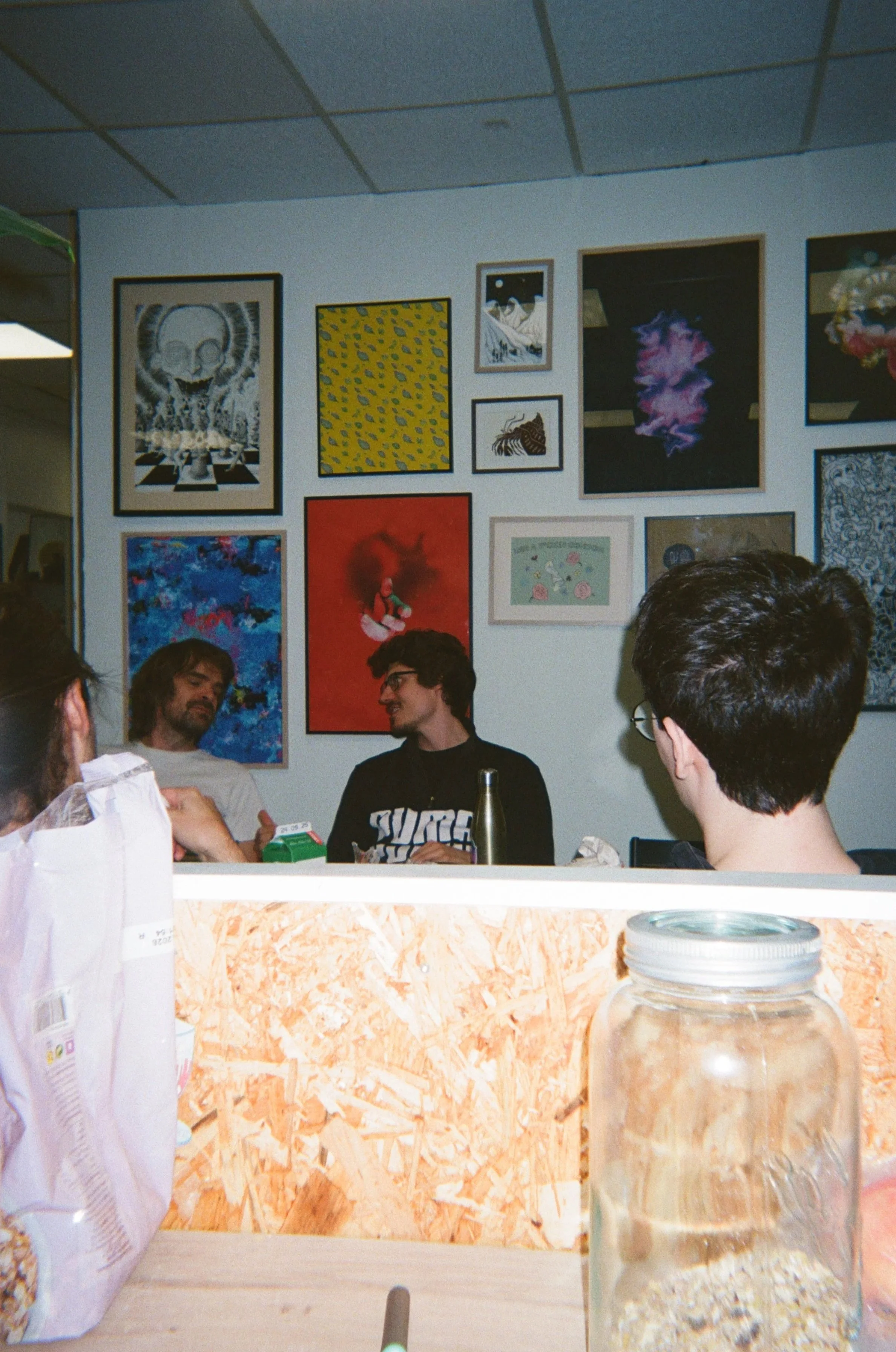 Et rom med tre personer som sitter og snakker. En vegg med flere fargerike kunstverk og fotografier henger på bakveggen.