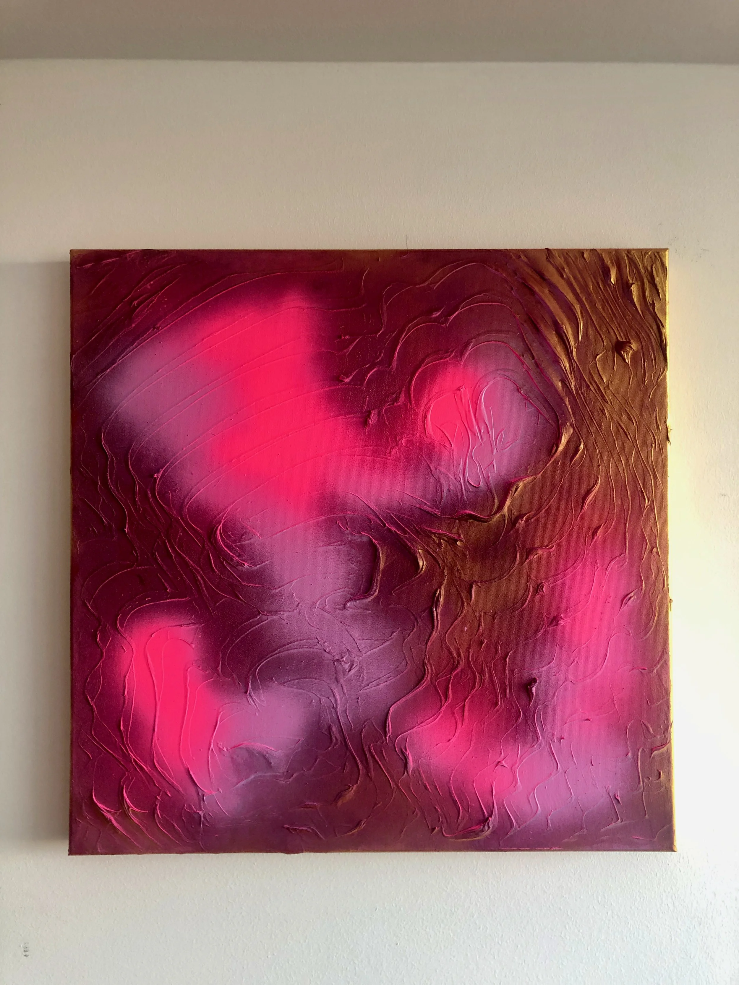 Close-up of a modern abstract painting with red and pink swirling patterns on a square canvas, mounted on a white wall.