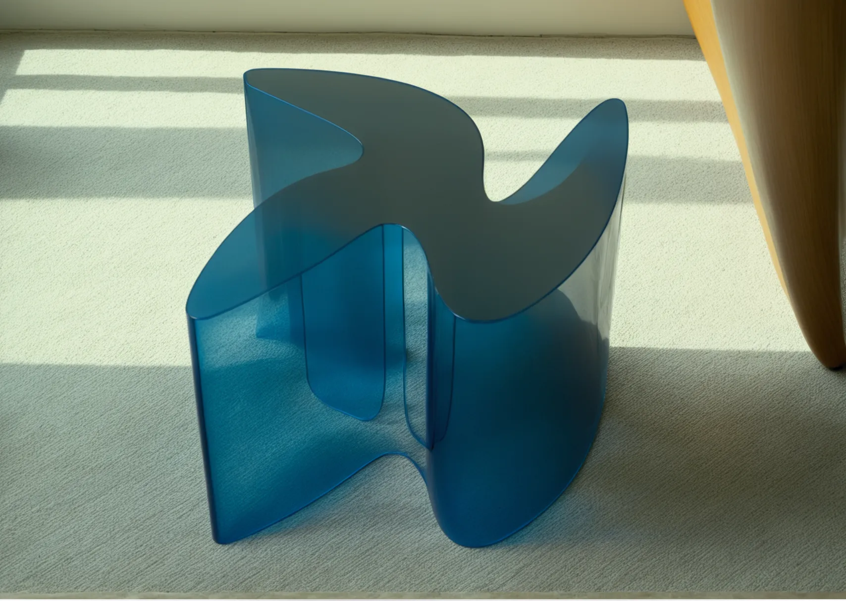 Modern blue abstract sculpture with smooth flowing curves, placed on a beige carpeted floor near a window with sunlight casting shadows.