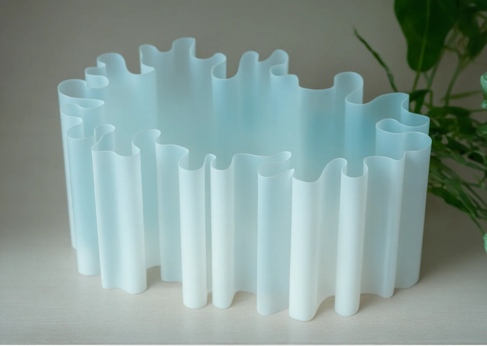 White, wavy, accordion-style plastic or acrylic object on a light surface, with green leaves in the background.