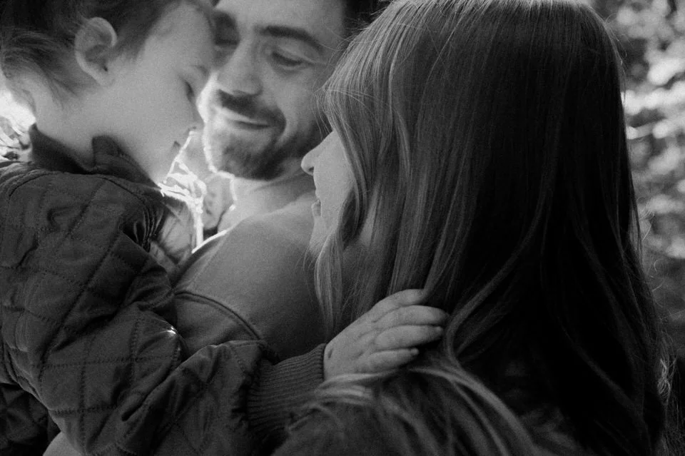 Black and white detail of parents gently holding their toddler during a family maternity photo session.