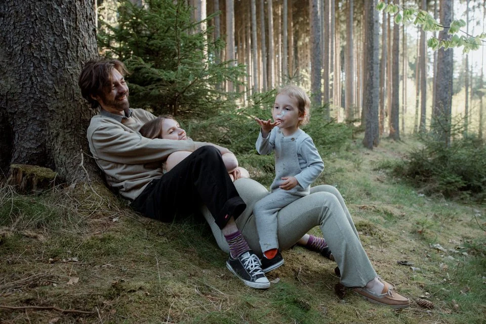 Toddler blowing into a feather during a natural outdoor family photoshoot in the forest.