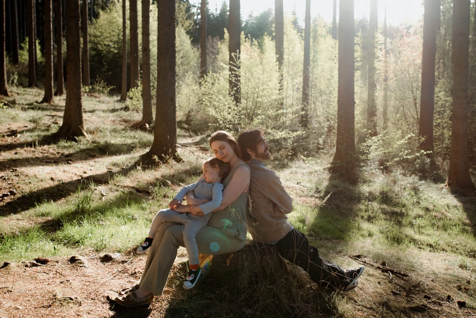 Family resting together on a tree stump in warm forest light during a relaxed outdoor photoshoot