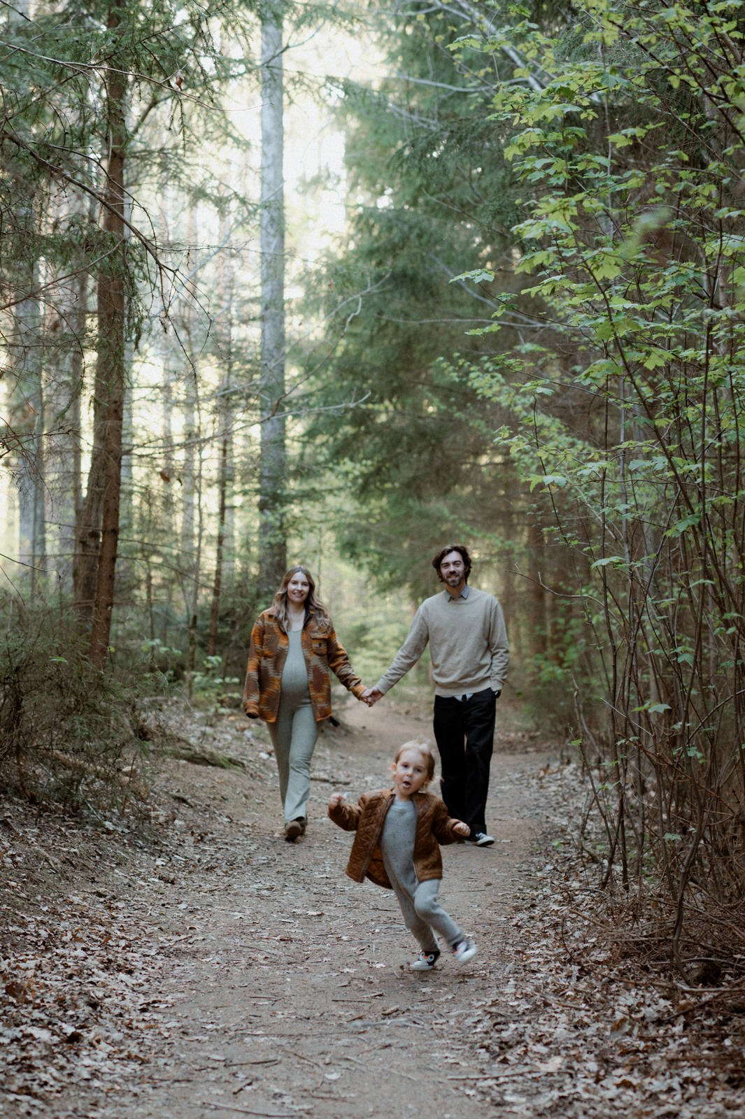 Family walking through a forest path near Vienna, with a toddler running ahead during a relaxed maternity and family photoshoot.