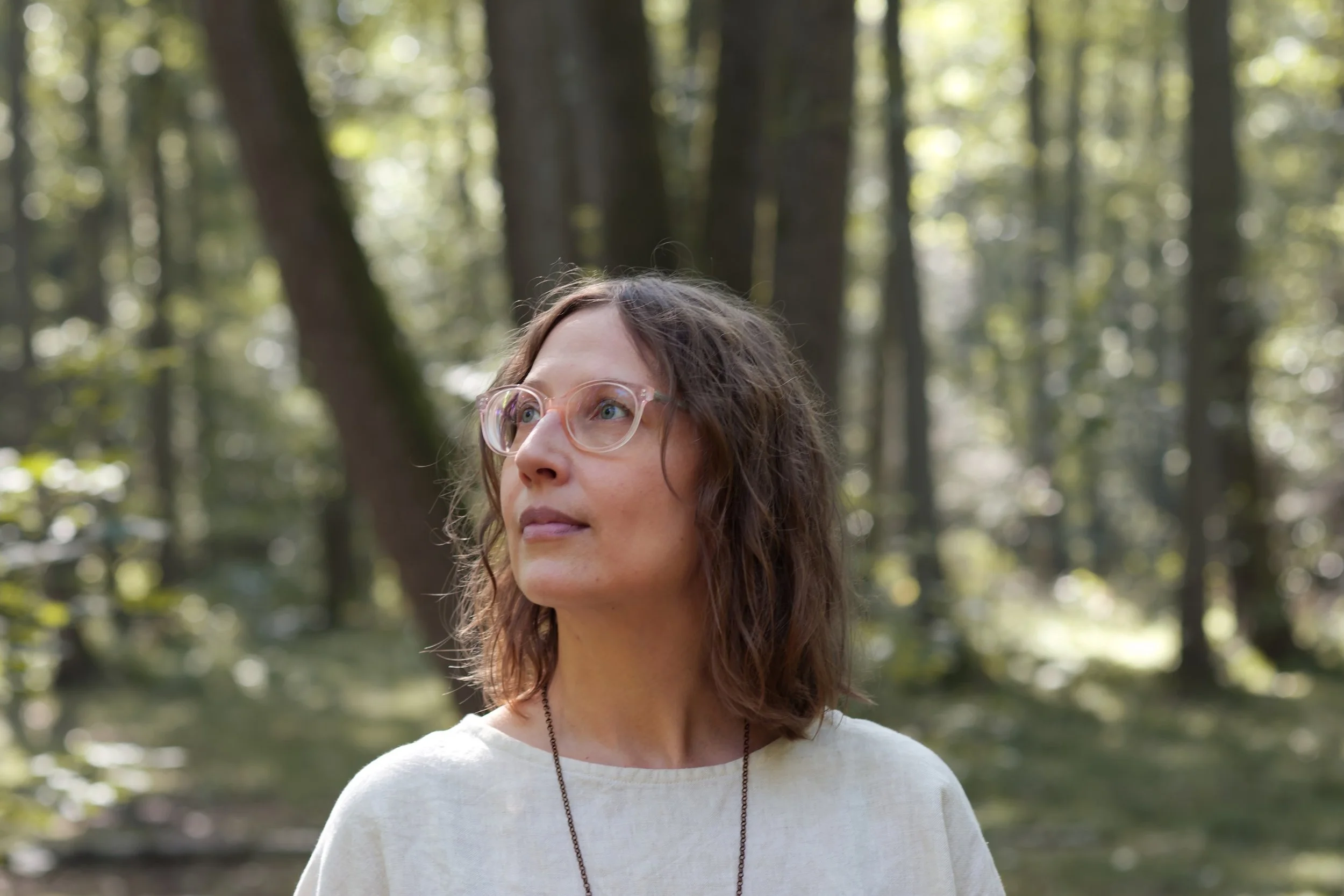 Eine Frau mit Brille in einem Wald, schaut nach oben.