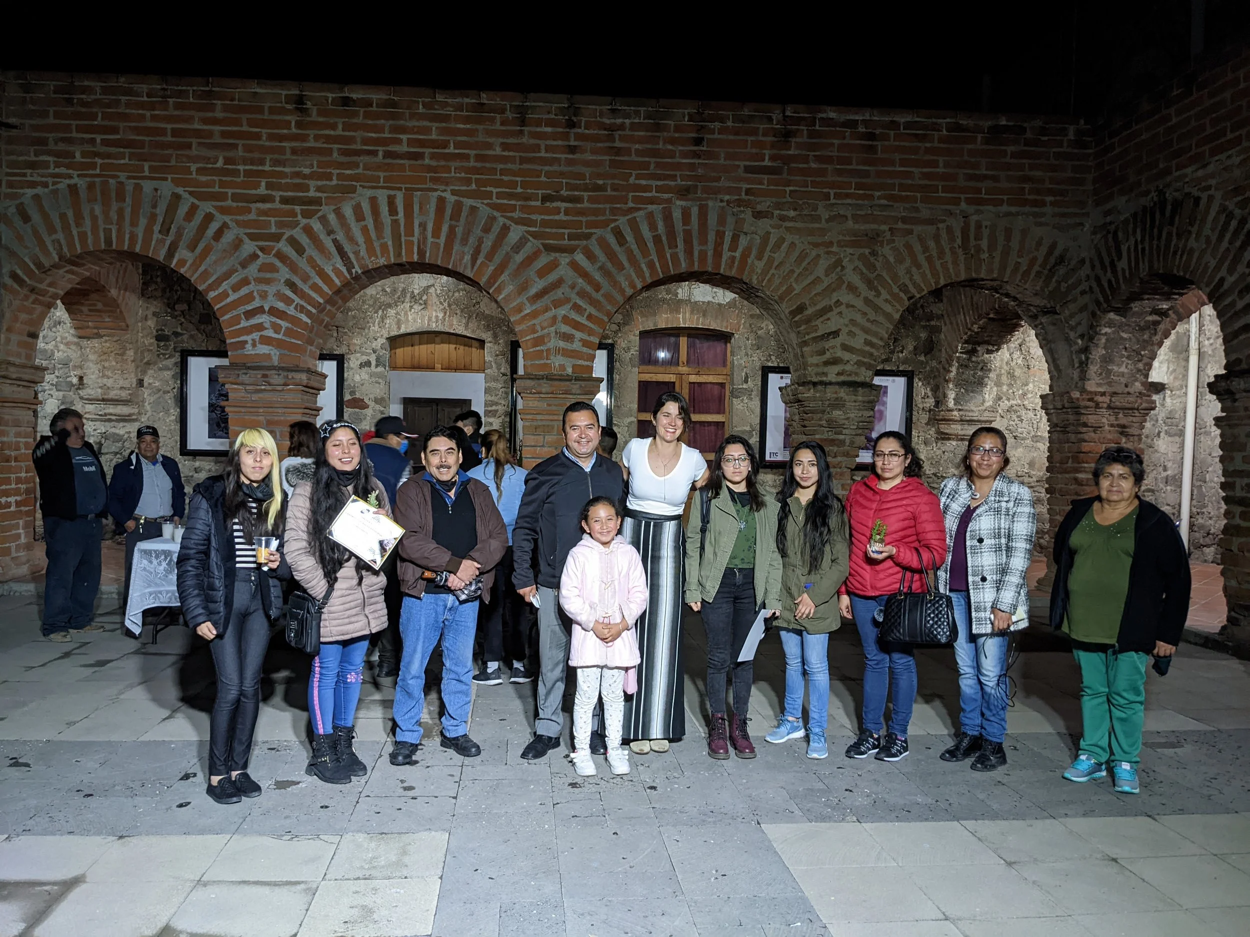 Group of people standing in front of a brick wall with arches inside an indoor or semi-indoor setting.