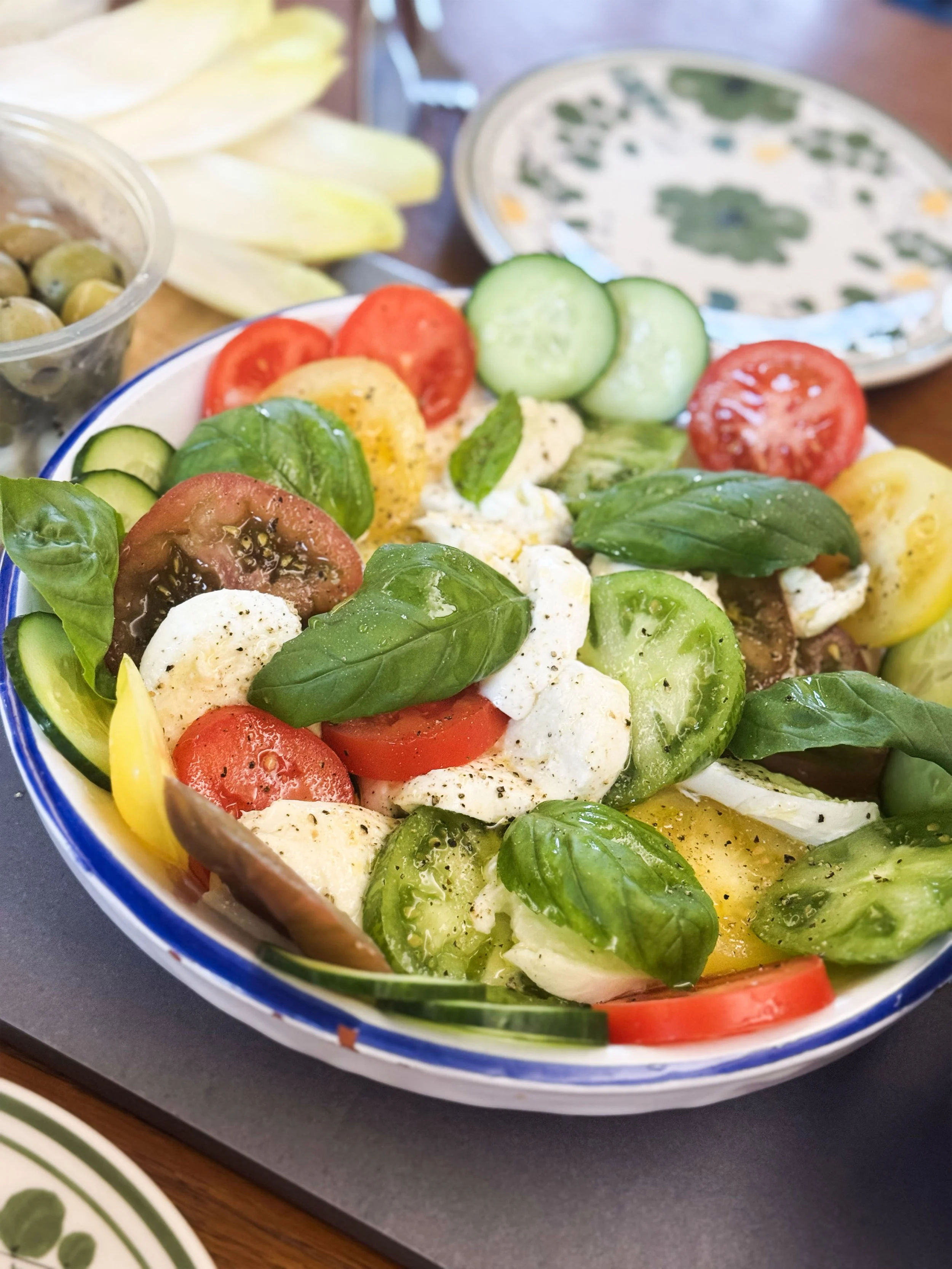 A colorful fresh salad with tomatoes, cucumbers, mozzarella cheese, basil, and yellow bell peppers in a ceramic bowl.
