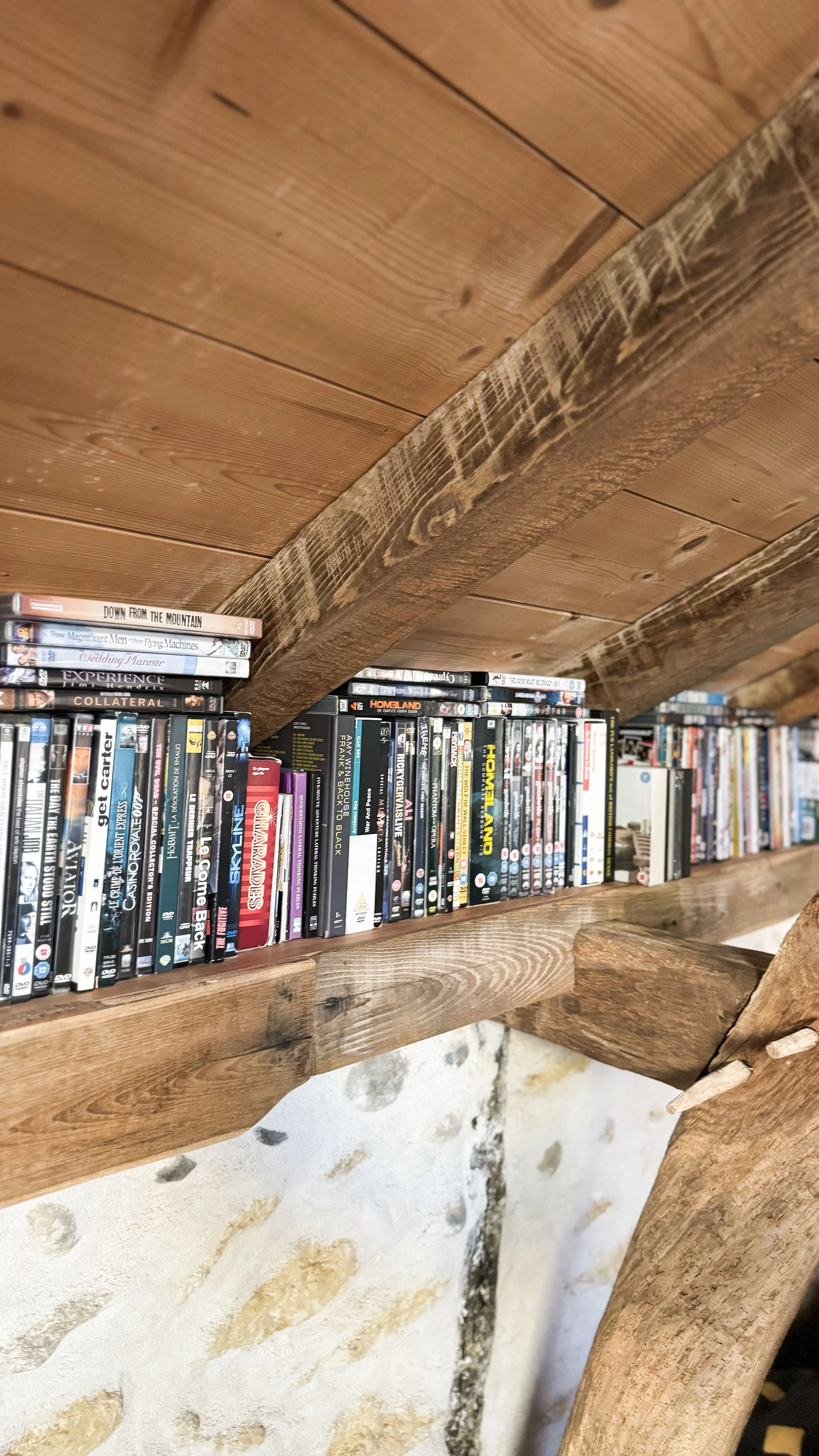 A wooden bookshelf filled with DVDs and Blu-ray discs, with a rustic wooden beam running across the top.