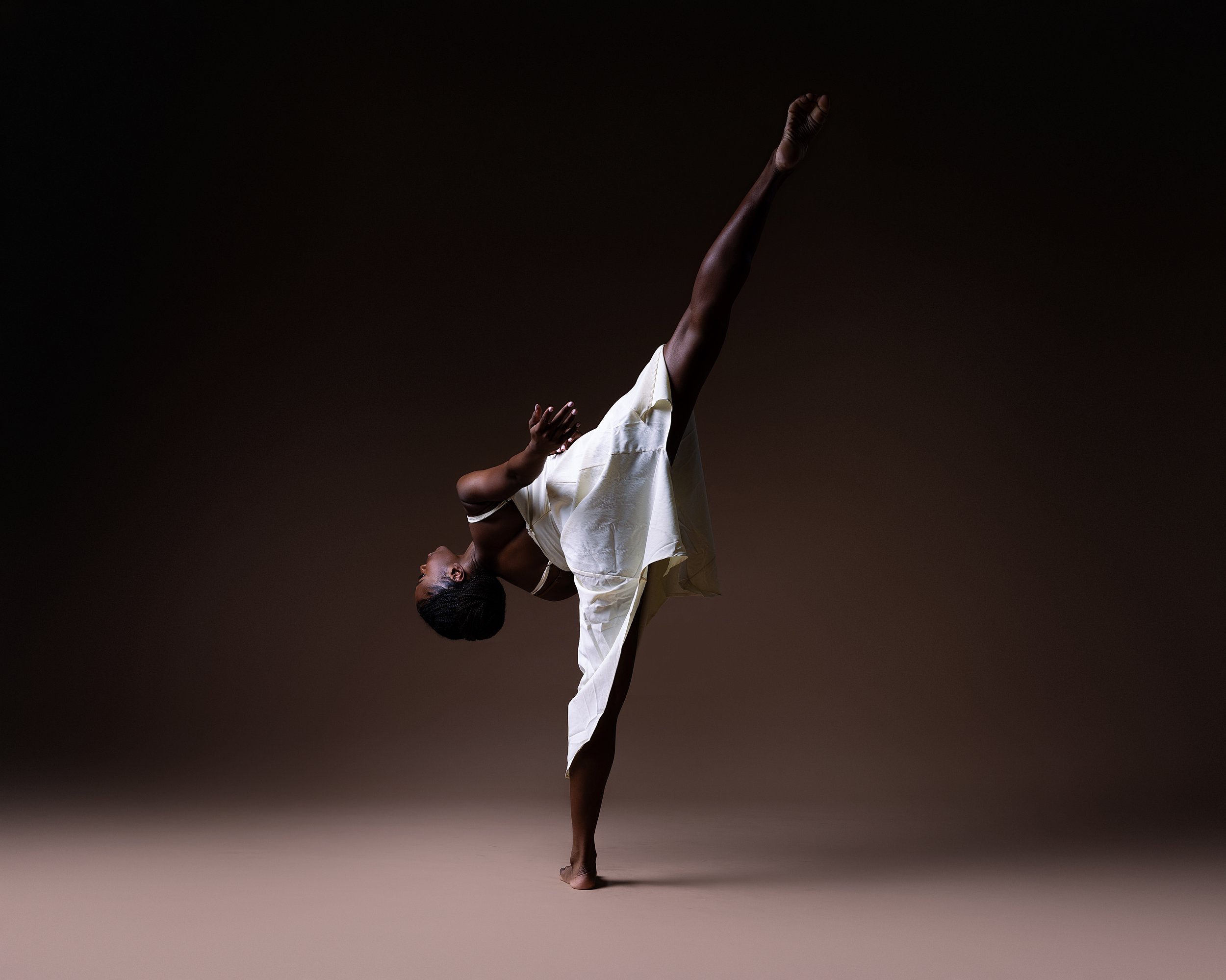 A person performing a one-handed yoga pose, balancing on one foot with the other leg extended upward, against a dark background.