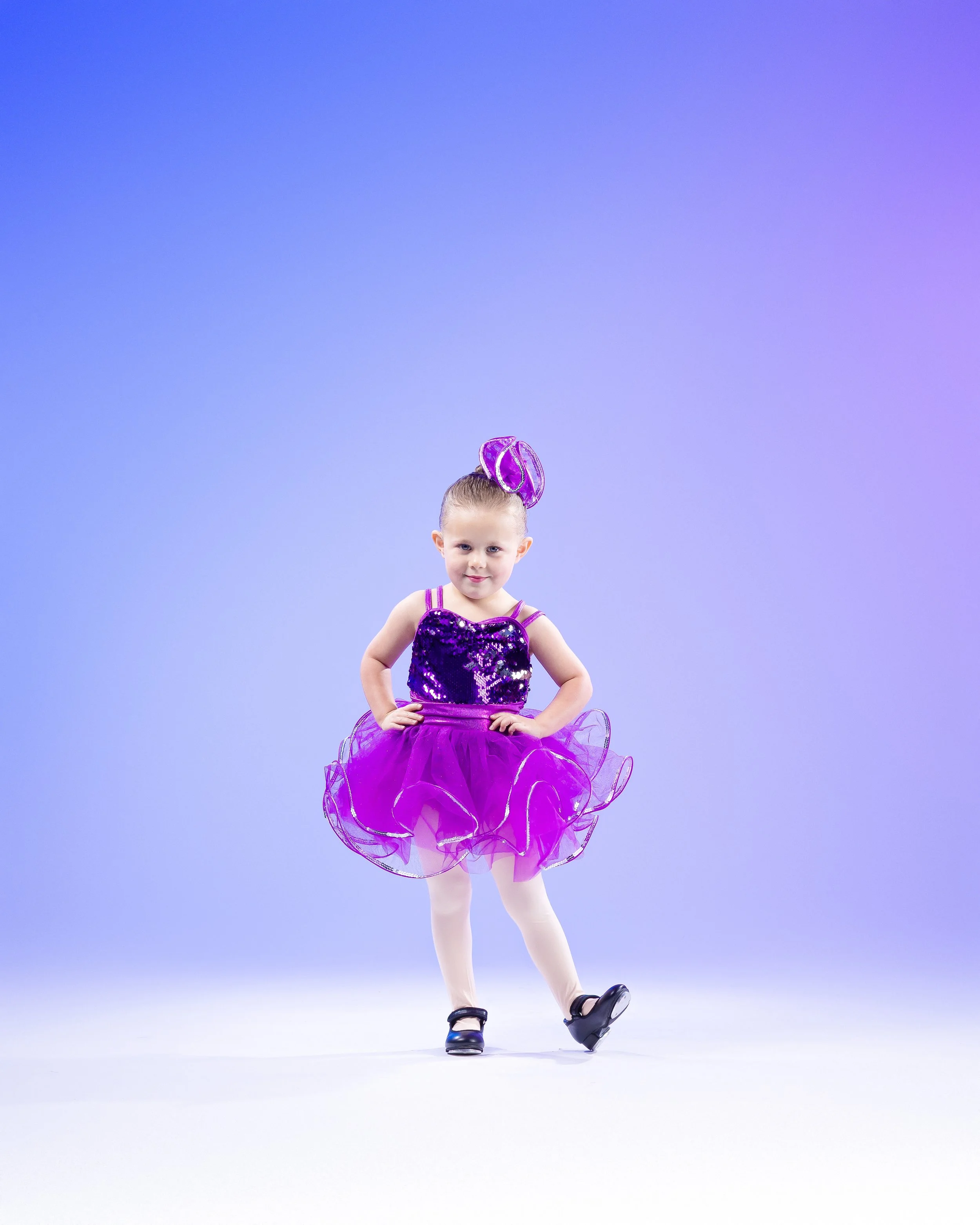 Young girl in a purple sequined costume standing on an ice skating rink.