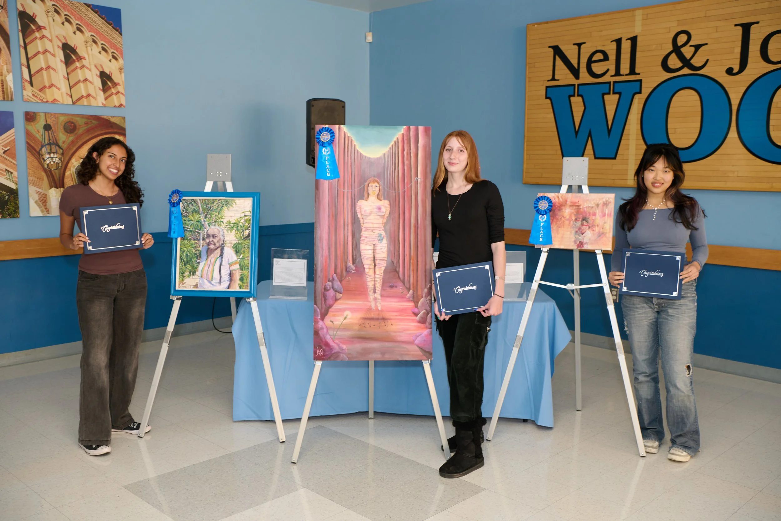 Three women each standing next to their winning artwork on easels.