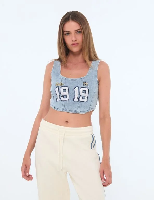 A woman modeling a denim cropped tank top featuring the year 1919.