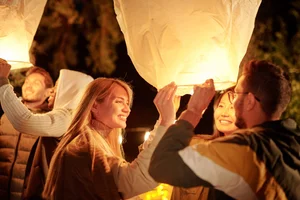 A group of people smiling as they prepare to release illuminated sky lanterns together during an outdoor evening cultural celebration