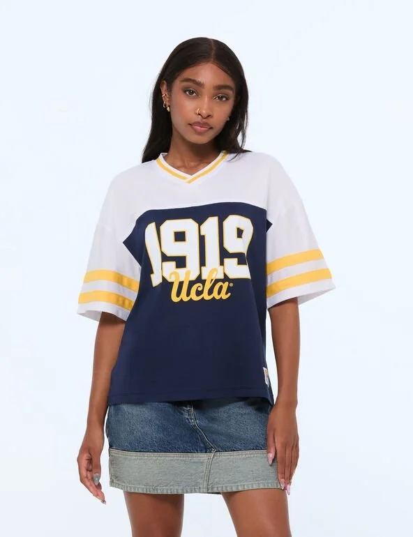 A woman wearing an oversized jersey featuring white, yellow and blue with the year 1919 behind the UCLA logo.