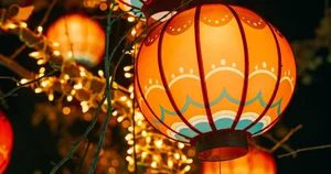 Decorative red and orange paper lanterns illuminated with warm lights, hanging outdoors at night during a cultural celebration
