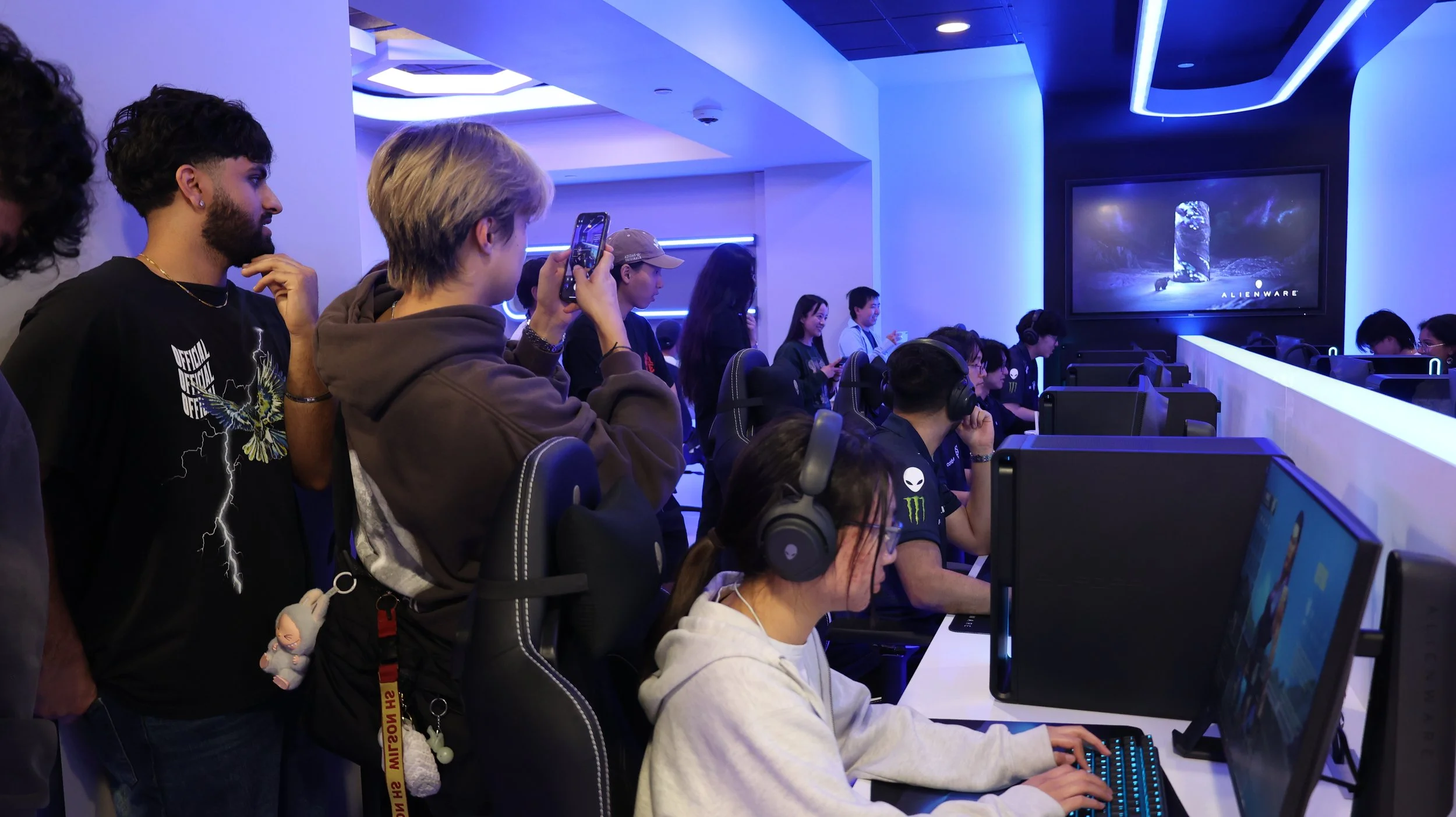 Students playing games, taking pictures of other students playing on desktops in a gaming lounge.
