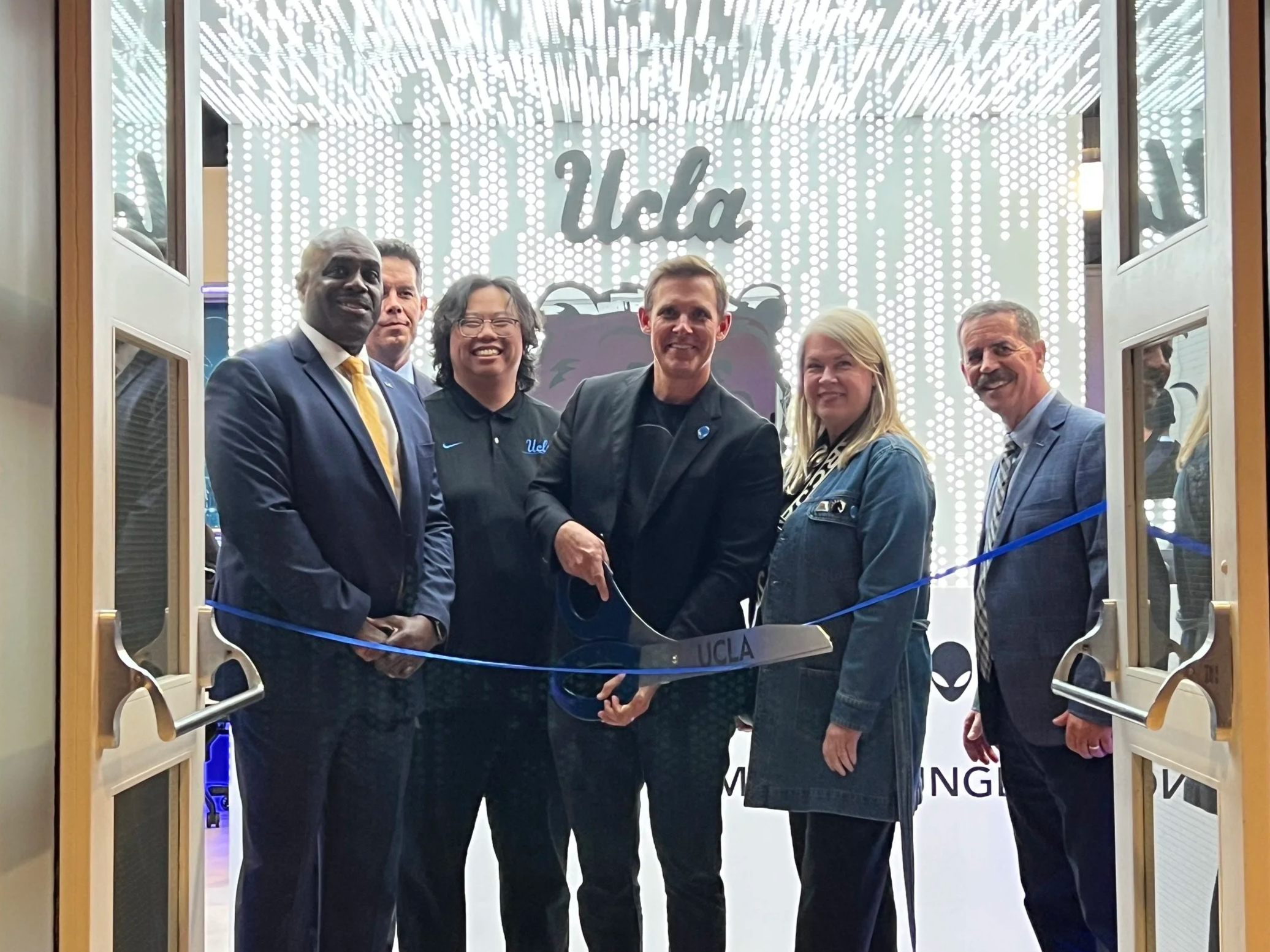 Five men and one woman cutting a blue ribbon to open the Bruin Esports Gamimg lounge at UCLA.