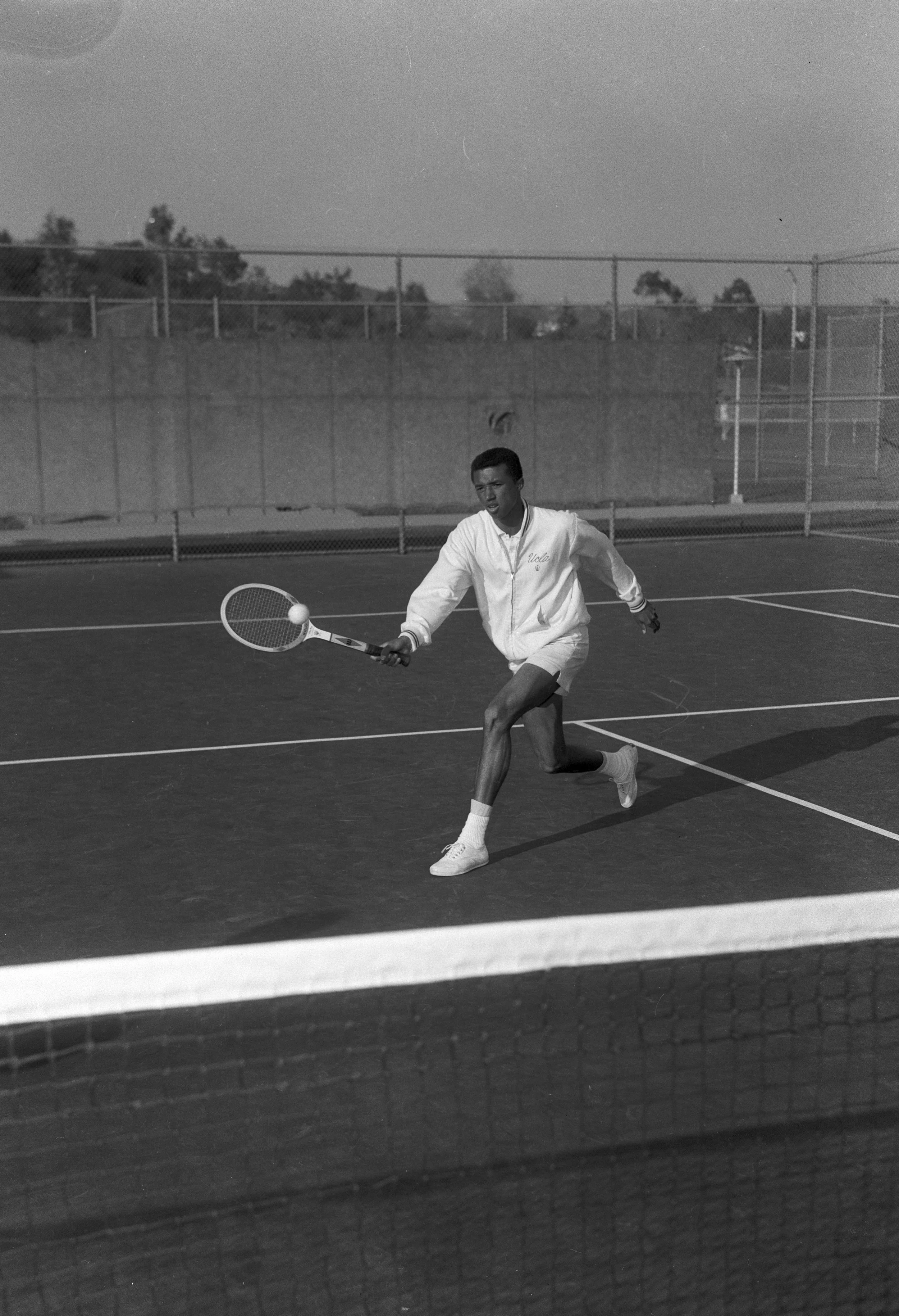Black and white image of man lunging toward tennis ball with racquet