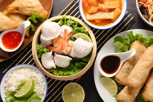 Overhead view of an assortment of Asian dishes, including shrimp dumplings, spring rolls, rice, soup, and dipping sauces, served with fresh lime wedges and lettuce