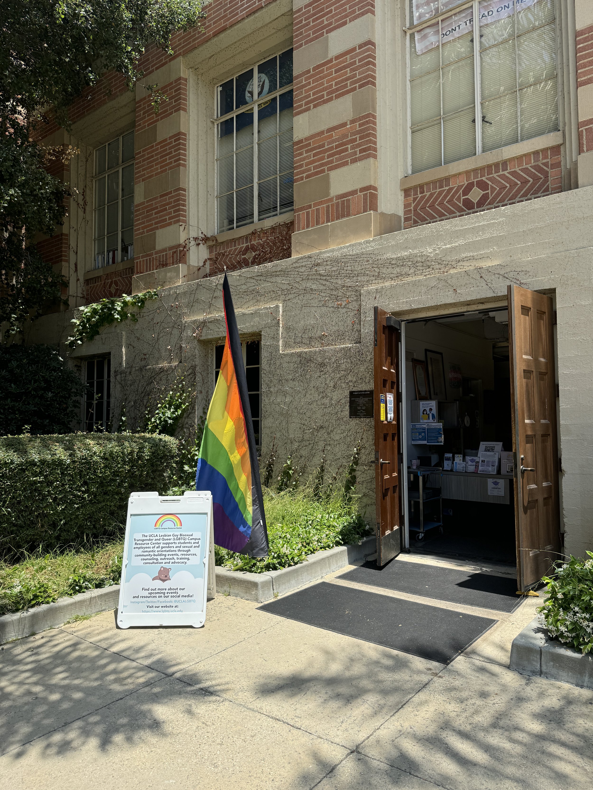 Office with brown open doors in brick building with rainbow flag and white A-frame sign outside