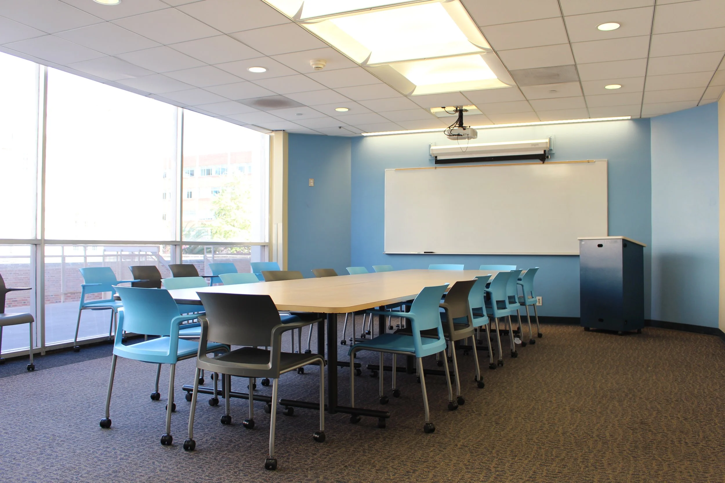 a UCLA conference space for rent. There's a long table with chairs all along the side, a whiteboard, projector and lectern.