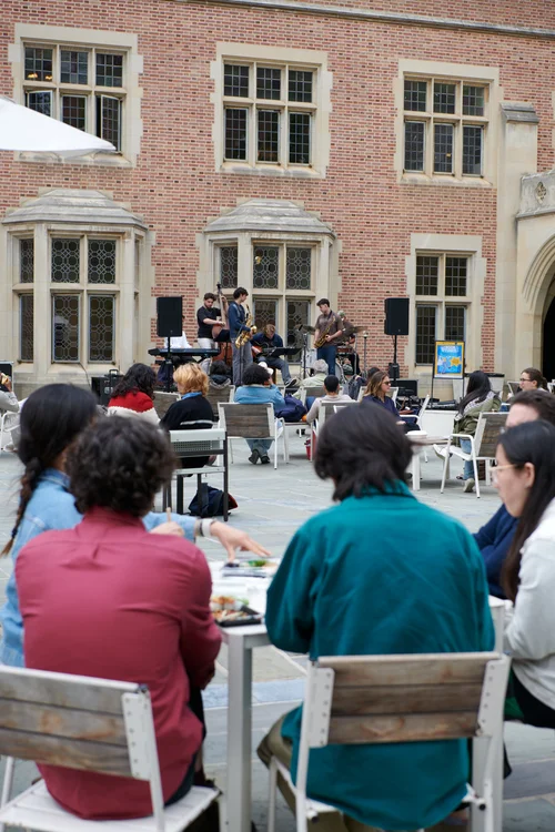 Students gather in a campus courtyard to watch a live band perform in front of a brick building