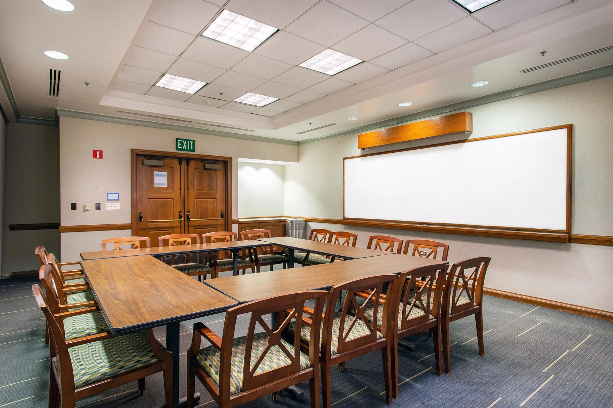 One of the Kerckhoff State Rooms, a conference room rental at UCLA. A brightly-lit room with tables arranged in a square, chairs around the tables. A whiteboard is mounted on the wall, and there's blue carpet on the floor.