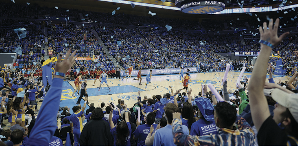 Fans in the foreground raise their hands to cheer on the UCLA basketball team during a game in UCLA's Pauley Pavilion.