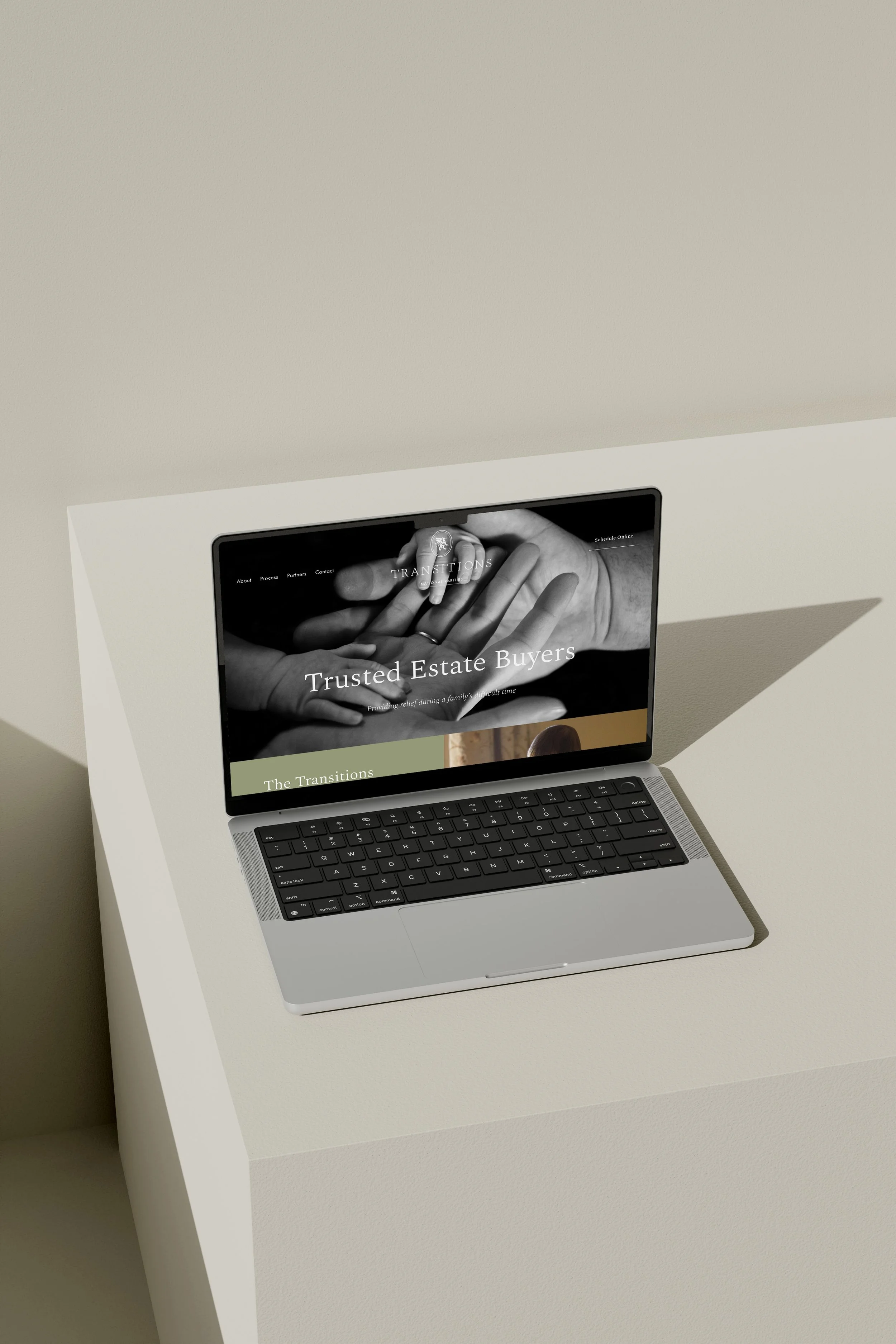 A laptop on a white table displaying a website titled "Trusted Estate Buyers" with an image of hands holding a key.