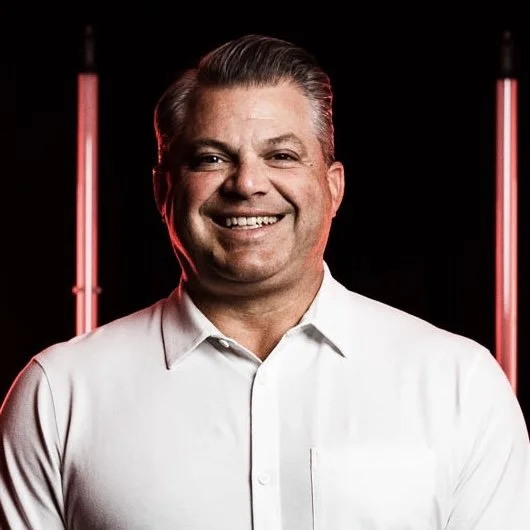 Smiling man in white shirt with red lights against dark background