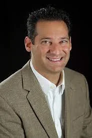 Smiling man in a brown suit against a dark background