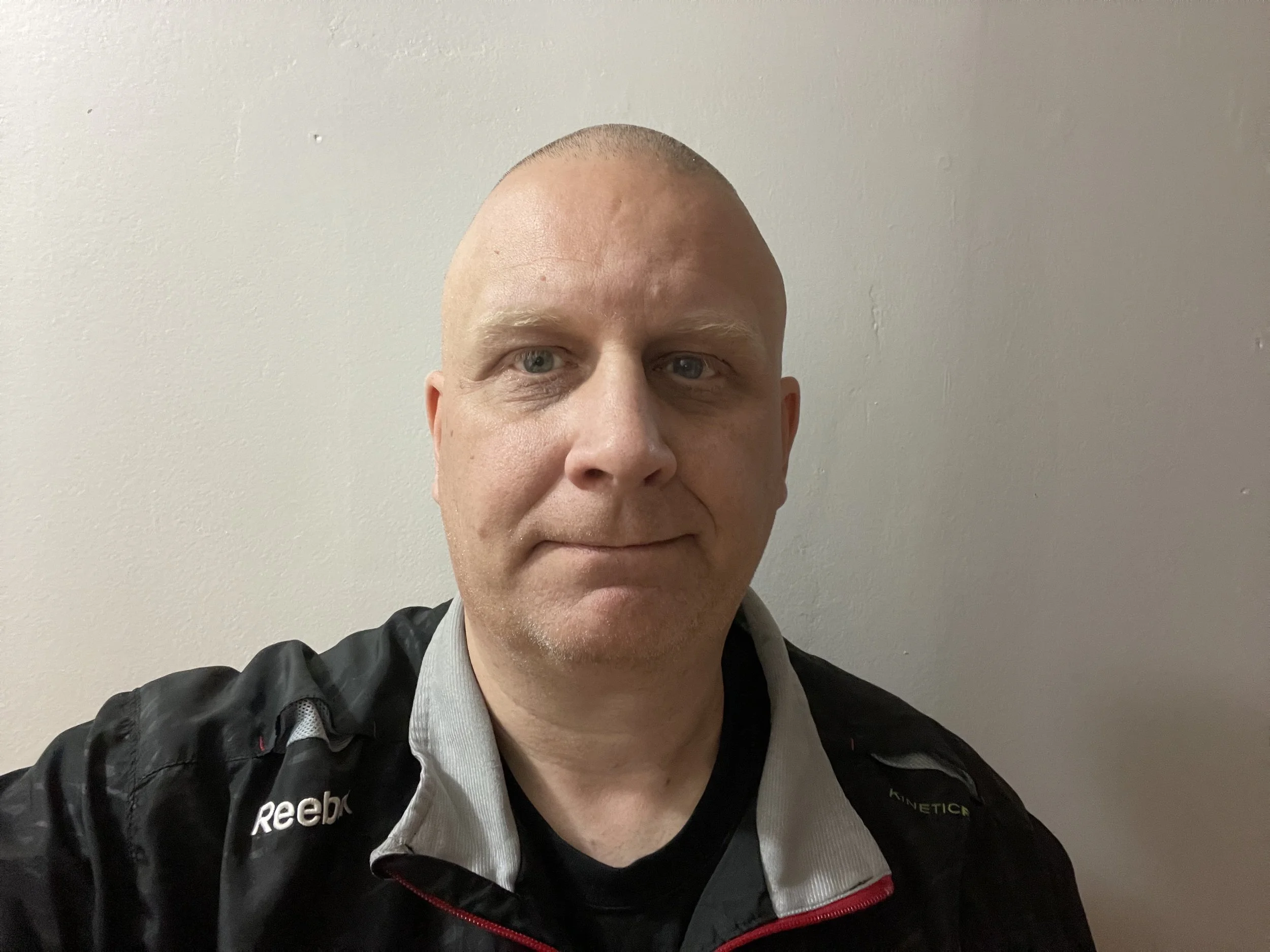 A person wearing a Reebok jacket standing against a plain wall.